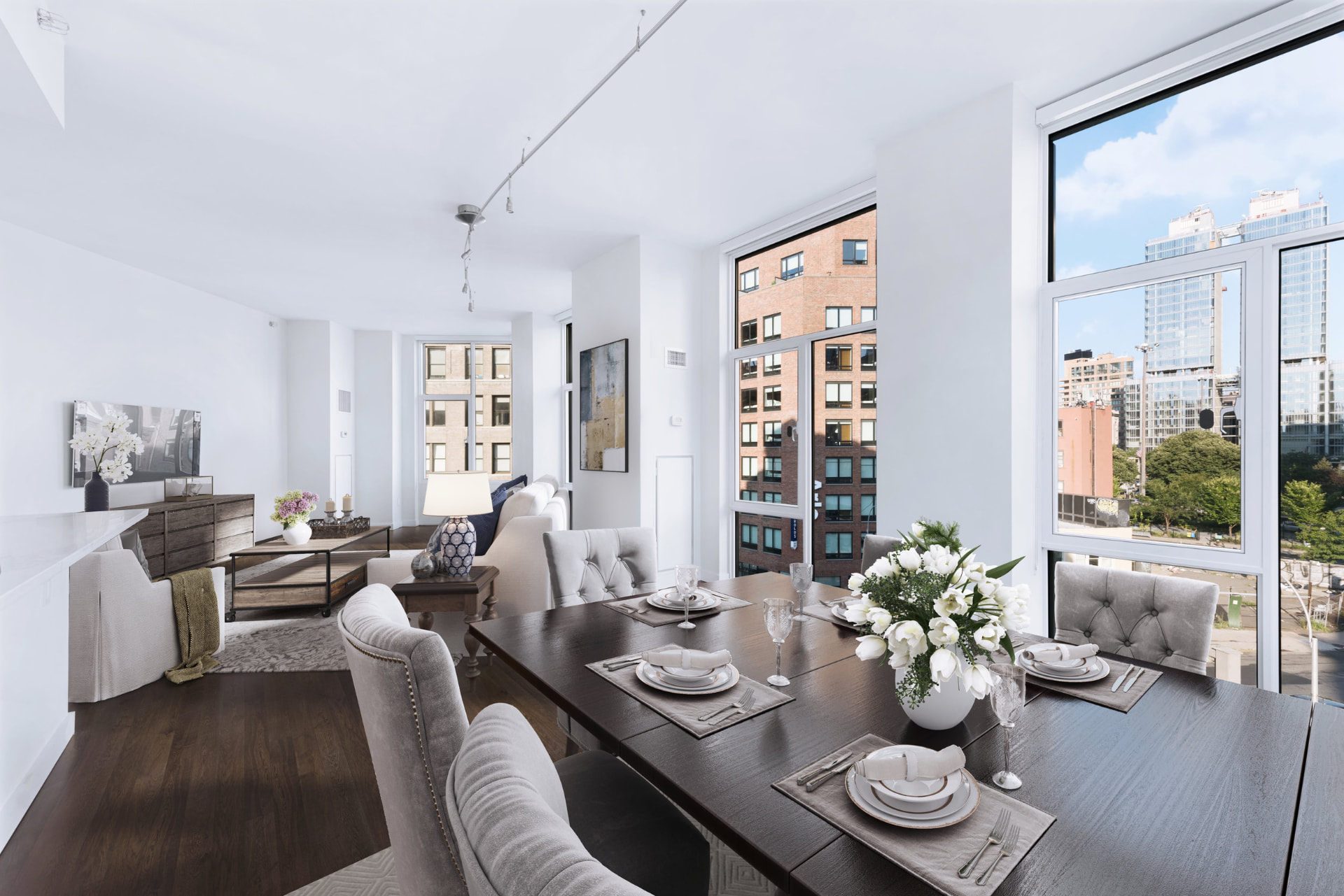 Tribeca II — dining room with a set table and upholstered chairs beside tall city-facing windows, with white built-in shelving and dark hardwood flooring — image 10 of 14