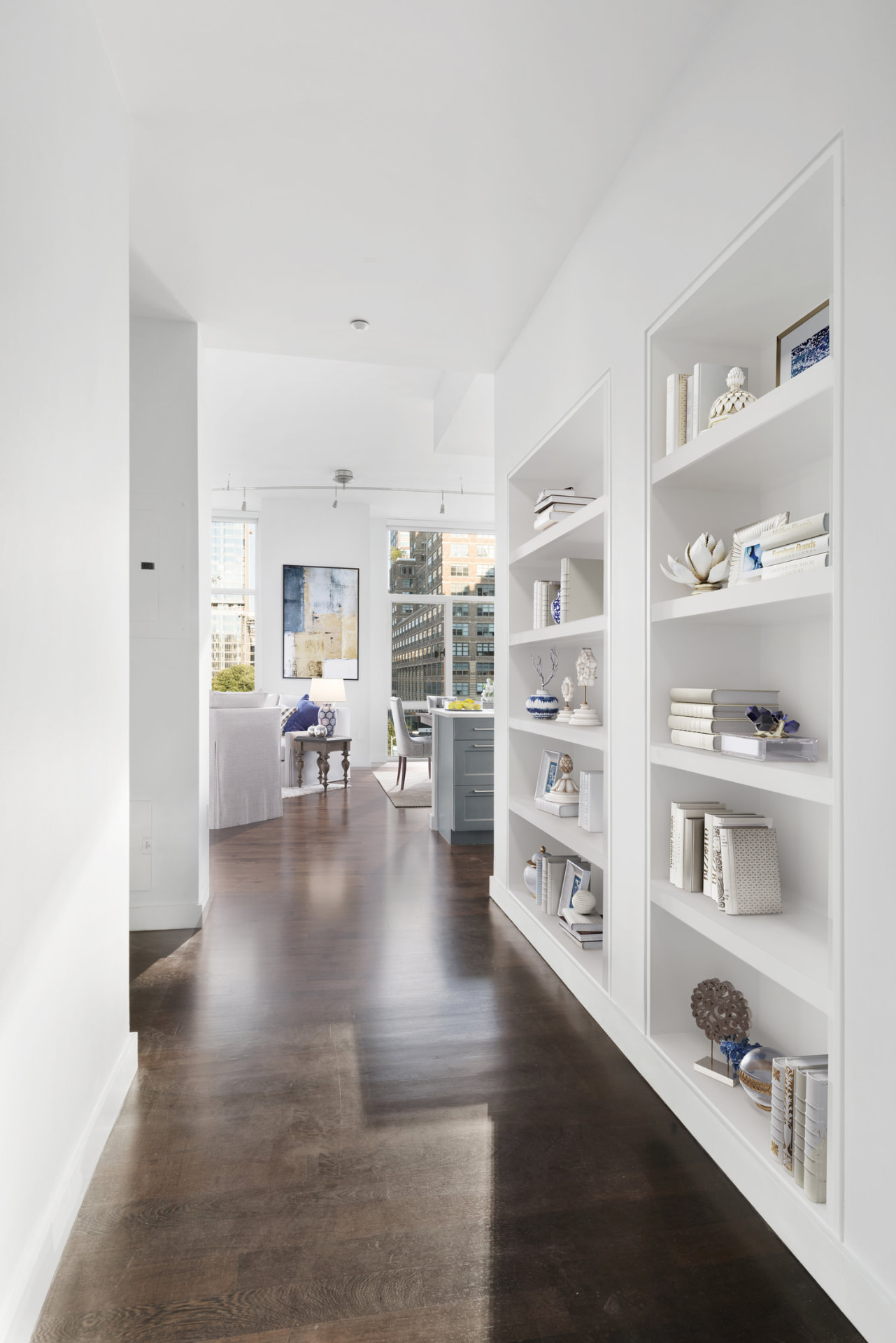 Tribeca II — dining room with a set table and upholstered chairs beside tall city-facing windows, with white built-in shelving and dark hardwood flooring — image 7 of 14