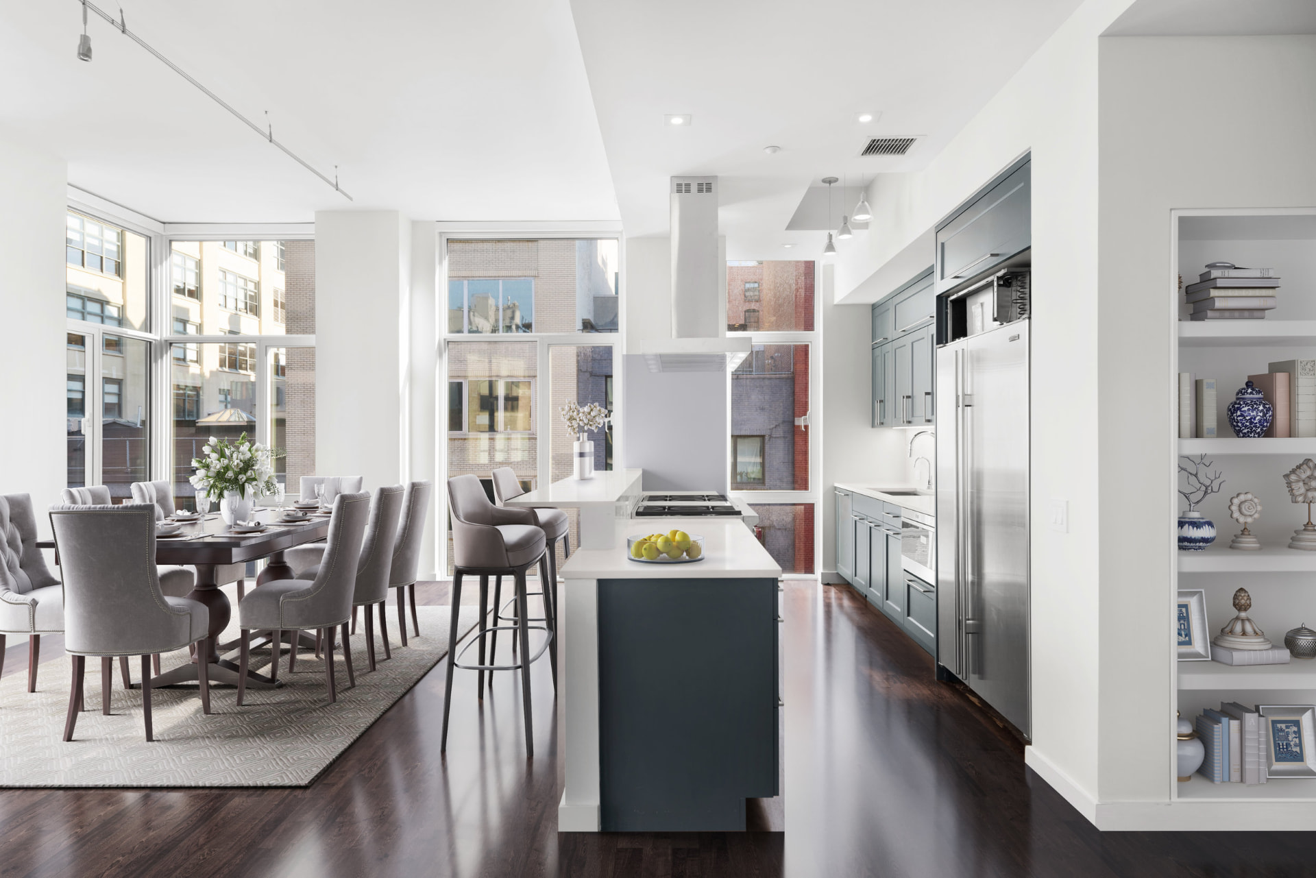 Tribeca II — dining room with a set table and upholstered chairs beside tall city-facing windows, with white built-in shelving and dark hardwood flooring — image 5 of 14