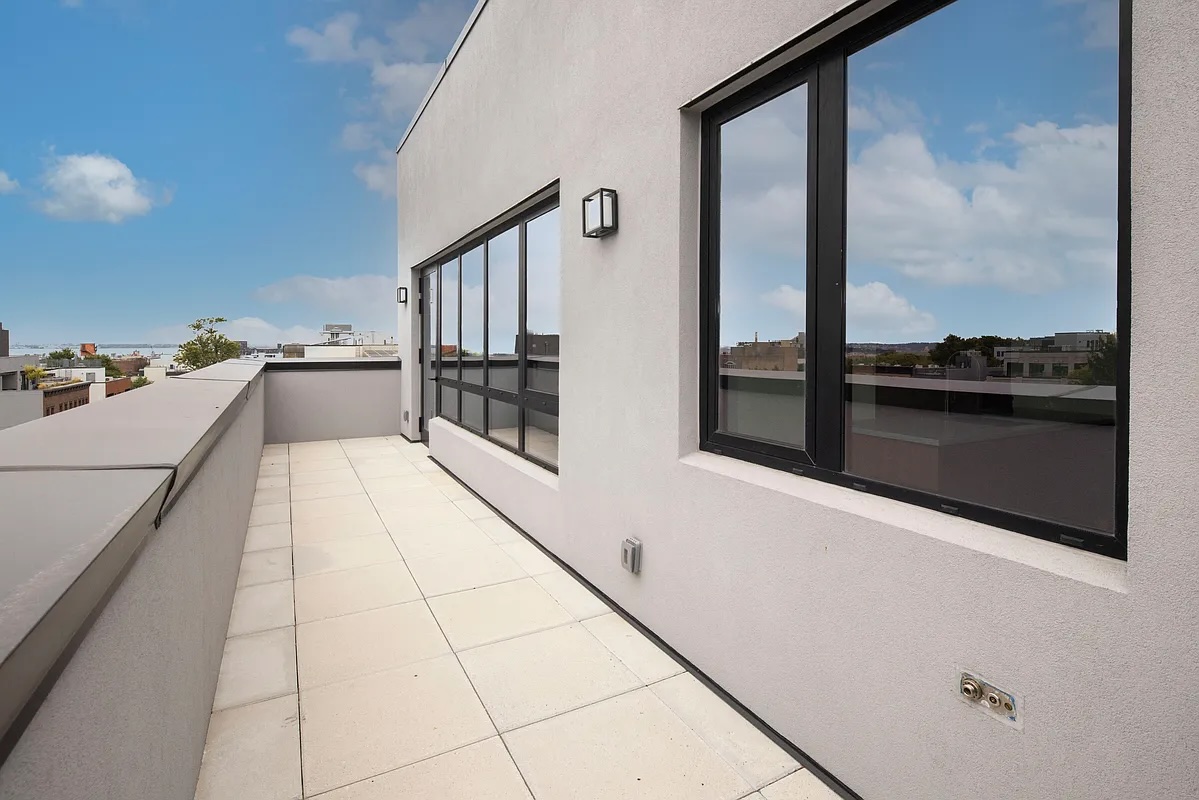 Greenwood Heights — narrow rooftop terrace with pale stone pavers alongside black-framed windows and a clear sky